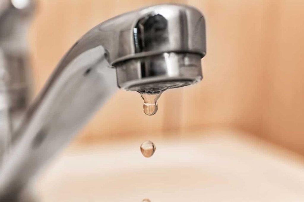 Vue d’un robinet qui goutte dans une cuisine, lumière naturelle diffusée, évocation du gaspillage d’eau domestique.