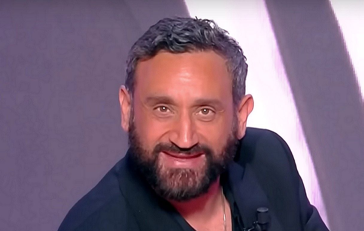 Portrait de l’animateur de télévision souriant, assis sur un plateau lumineux, filmé en gros plan avec micro accroché à sa veste.