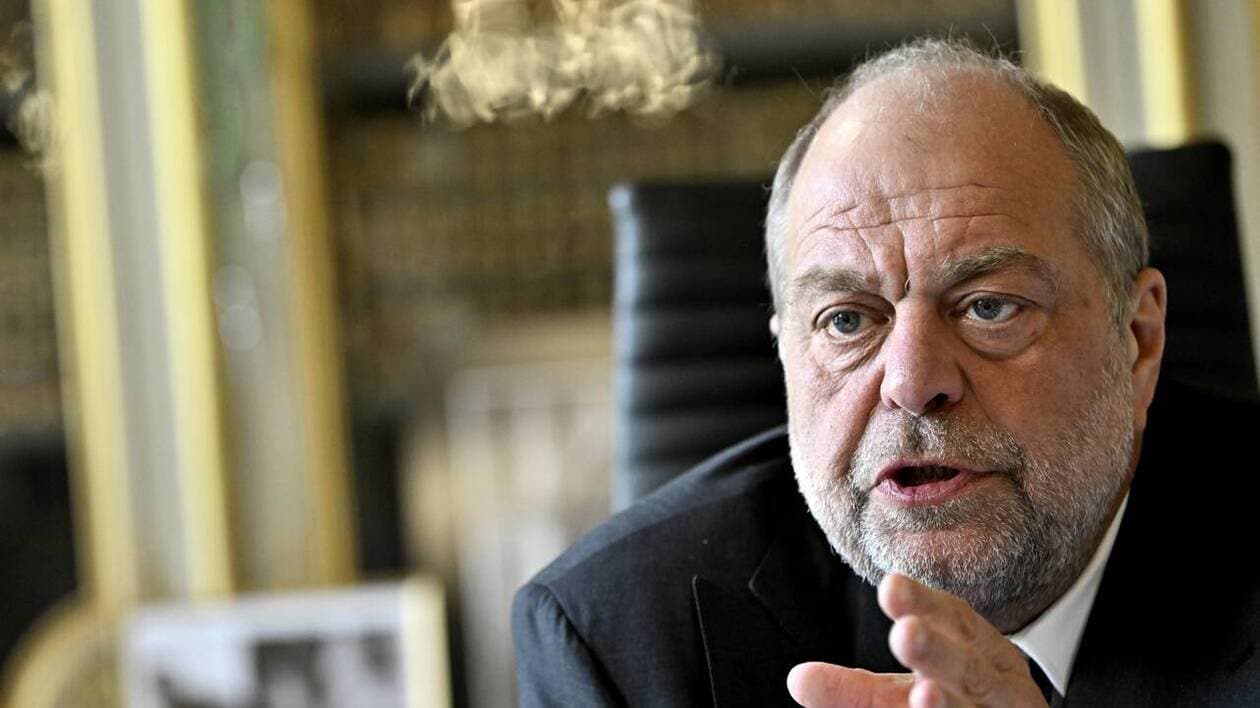 Un homme mûr en costume sombre, assis à son bureau, le regard grave et concentré, s’exprimant avec intensité, symbolisant la réflexion et le poids d’un souvenir douloureux.