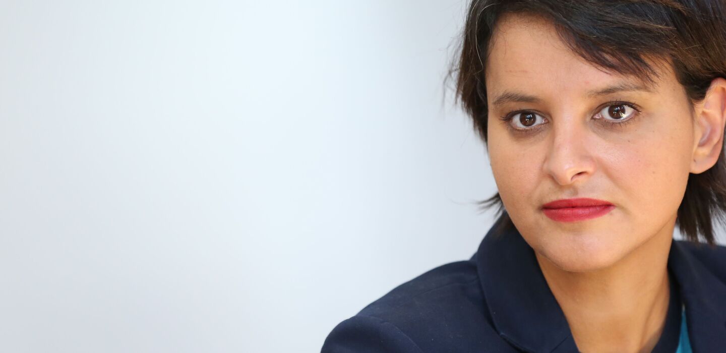 Portrait d’une femme au regard sérieux, vêtue d’une veste sombre, sur fond clair et épuré.