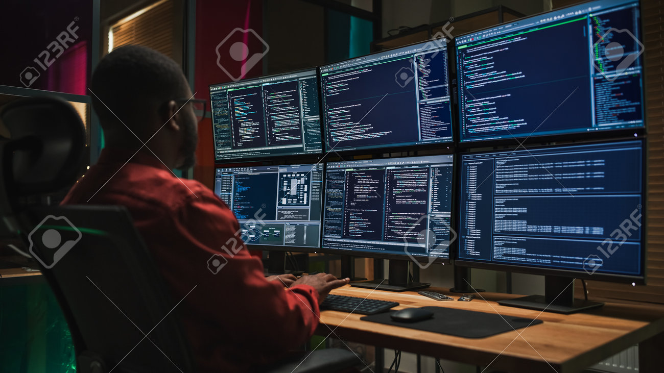 Homme assis devant plusieurs écrans d’ordinateur affichant des lignes de code, représentant une enquête informatique ou une activité de cybersécurité dans un bureau sombre.
