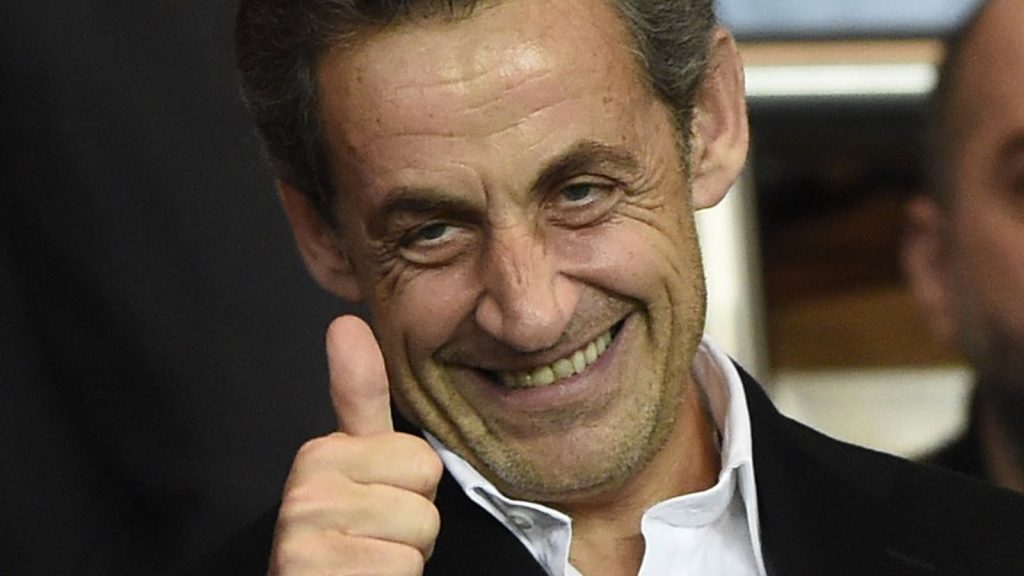 Homme souriant en costume sombre levant le pouce en signe d’approbation, éclairage intérieur chaleureux, ambiance conviviale et positive.