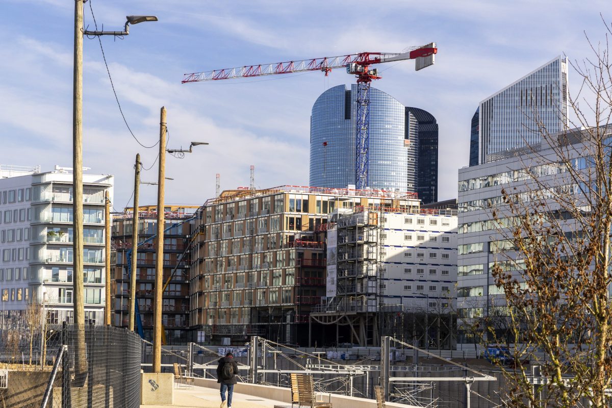 Vue d’un quartier du nord de Paris avec des immeubles modernes en construction, une grande grue rouge et blanche, des tours de bureaux en arrière-plan et une personne marchant sur une passerelle au premier plan, illustrant l’évolution urbaine du secteur.