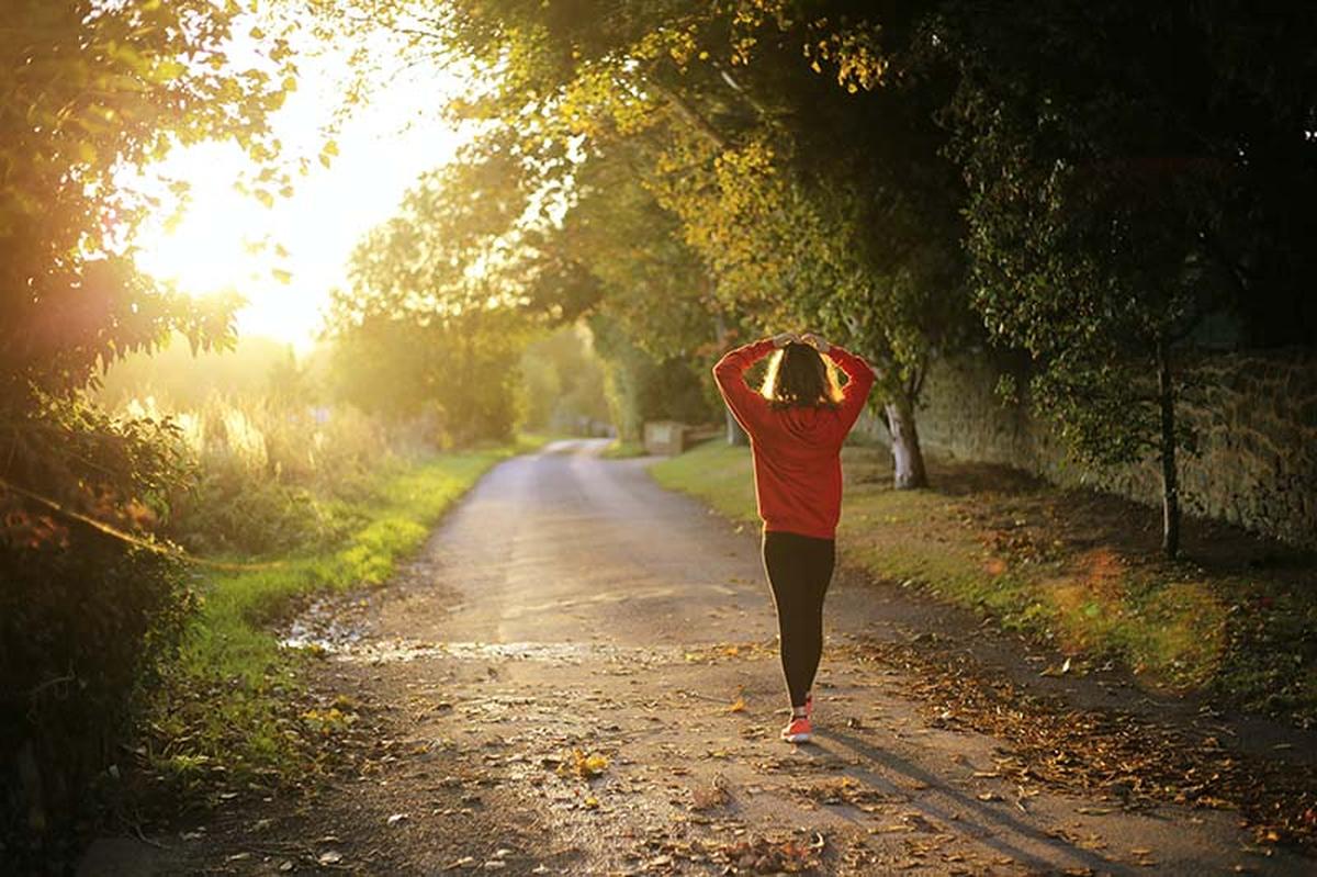Personne marchant seule sur un chemin en pleine nature au lever du soleil, illustrant une marche rapide utilisée pour perdre du poids, améliorer la santé et favoriser le bien-être.