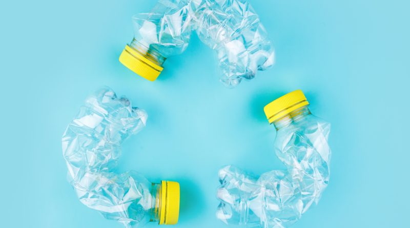 Trois bouteilles en plastique transparent écrasées avec bouchon jaune, disposées en cercle sur un fond bleu, symbolisant le recyclage et la question du compactage des bouteilles avant tri.
