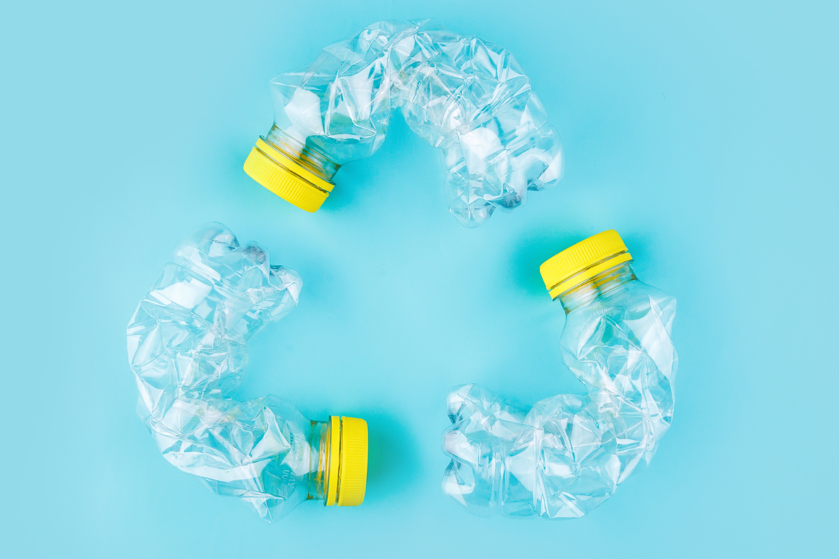 Trois bouteilles en plastique transparent écrasées avec bouchon jaune, disposées en cercle sur un fond bleu, symbolisant le recyclage et la question du compactage des bouteilles avant tri.