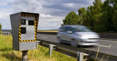 Radar automatique installé en bord de route avec un véhicule flou passant à vitesse modérée, environnement rural, ciel nuageux, scène illustrant la surveillance routière et le contrôle de vitesse