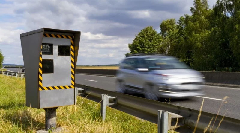 Radar automatique installé en bord de route avec un véhicule flou passant à vitesse modérée, environnement rural, ciel nuageux, scène illustrant la surveillance routière et le contrôle de vitesse