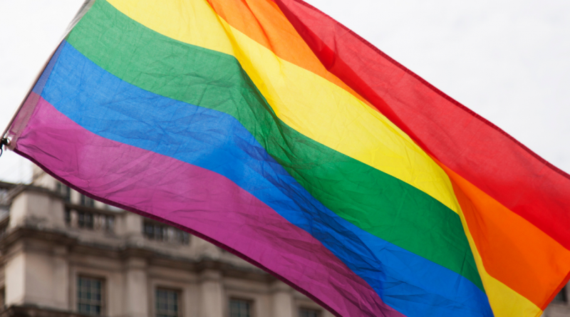 Drapeau arc-en-ciel flottant dans le vent devant un bâtiment ancien.