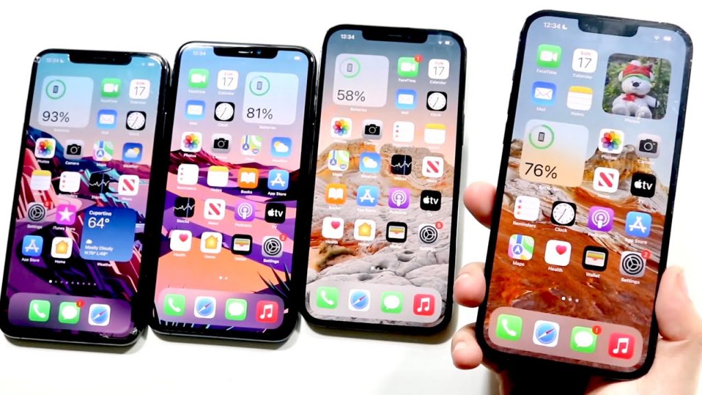 Quatre smartphones modernes alignés côte à côte, écrans allumés, montrant des interfaces similaires avec icônes colorées et niveaux de batterie visibles.