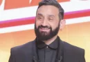 Animateur barbu souriant en costume sombre sur un plateau lumineux, évoquant une prise de parole médiatique et une confidence publique