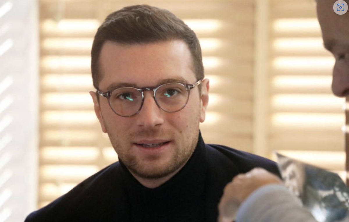 Jeune homme politique portant des lunettes, regard sérieux, en entretien dans un intérieur lumineux aux tons neutres