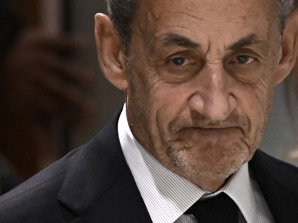 Visage d’un homme âgé en costume sombre, expression fermée, éclairage neutre en intérieur.