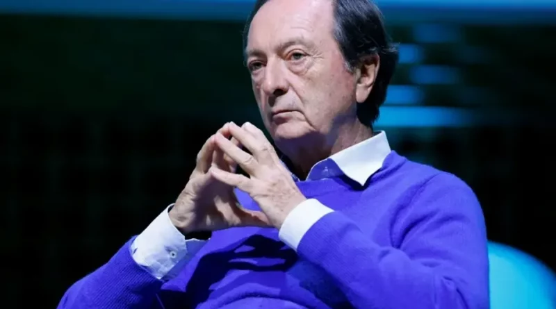 Personne assise en intérieur, mains jointes, posture sérieuse, éclairage bleu.