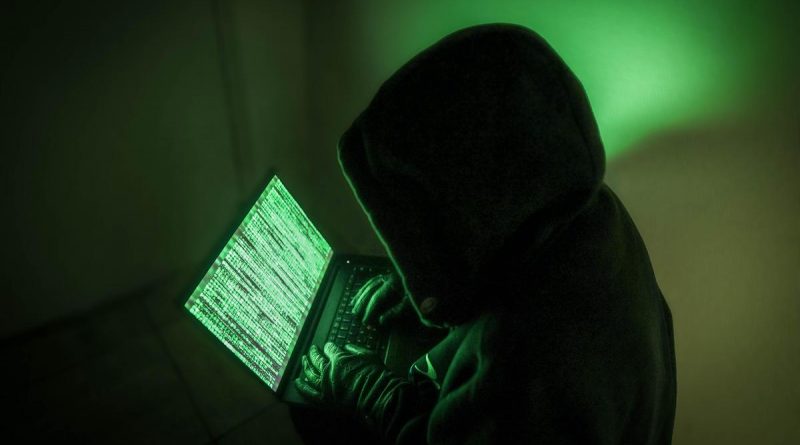 Silhouette encapuchonnée utilisant un ordinateur portable dans une ambiance sombre et verdâtre, symbolisant un piratage informatique et une intrusion dans des données personnelles sensibles