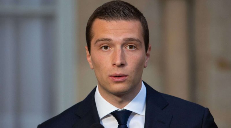 Jeune responsable politique en costume sombre, debout derrière un pupitre, regard sérieux face à l’objectif, dans un cadre institutionnel.