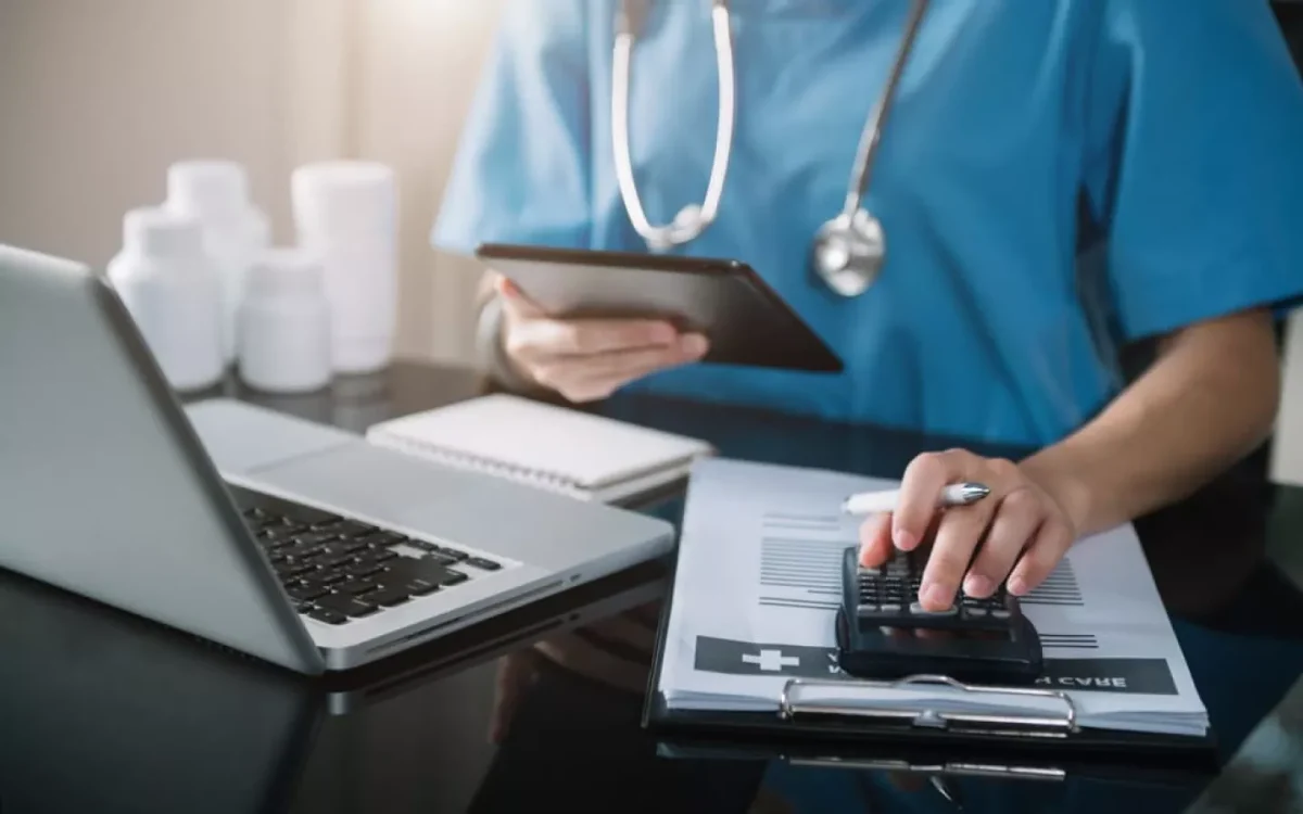 Professionnel de santé en tenue médicale consultant des documents de remboursement et calculant les frais de soins sur un bureau
