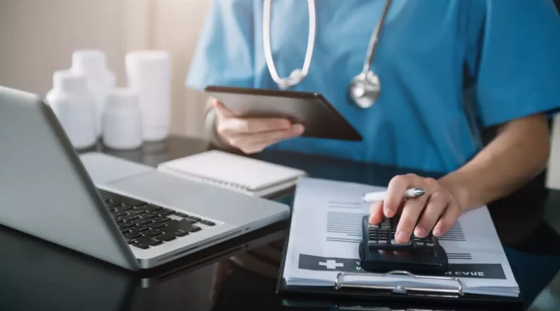 Professionnel de santé en tenue médicale consultant des documents de remboursement et calculant les frais de soins sur un bureau