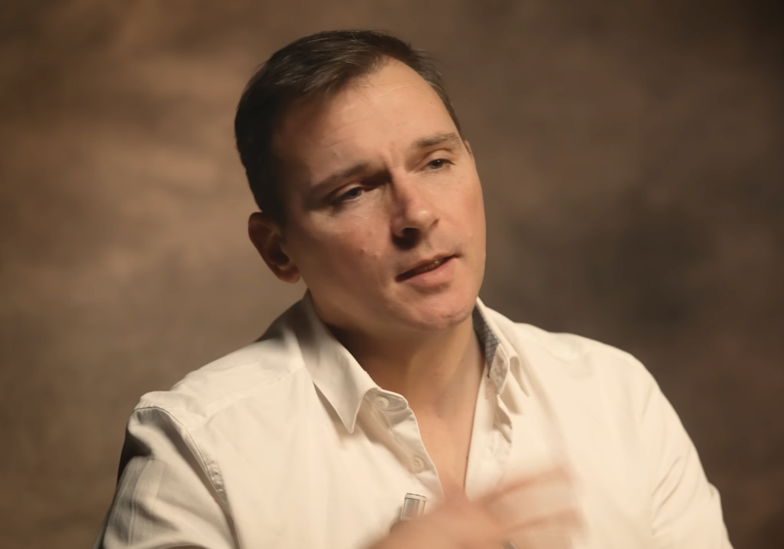 Personne filmée en intérieur, portant une chemise claire, parlant face à la caméra dans une ambiance lumineuse douce et chaleureuse.