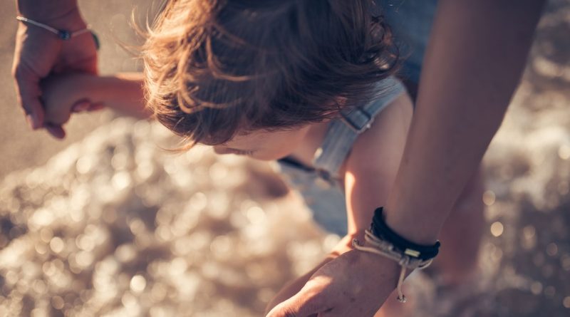 Enfant tenant la main d’un adulte au bord de l’eau, éclairé par une lumière douce.