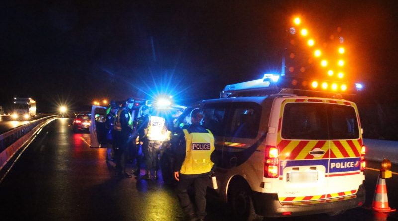 Contrôle routier nocturne avec forces de l’ordre intervenant sur une voie rapide, gyrophares allumés et signalisation lumineuse indiquant un danger après une alcoolémie extrême