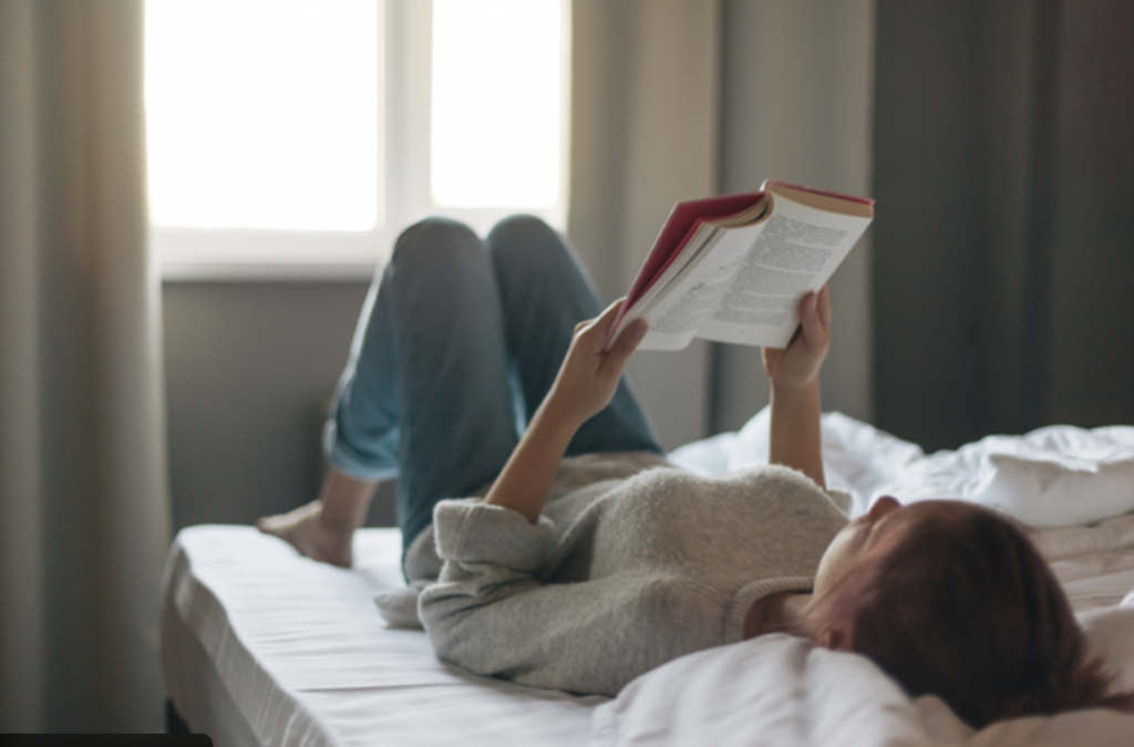 Personne allongée sur un lit lisant un livre pendant un arrêt maladie, en tenue décontractée, à son domicile