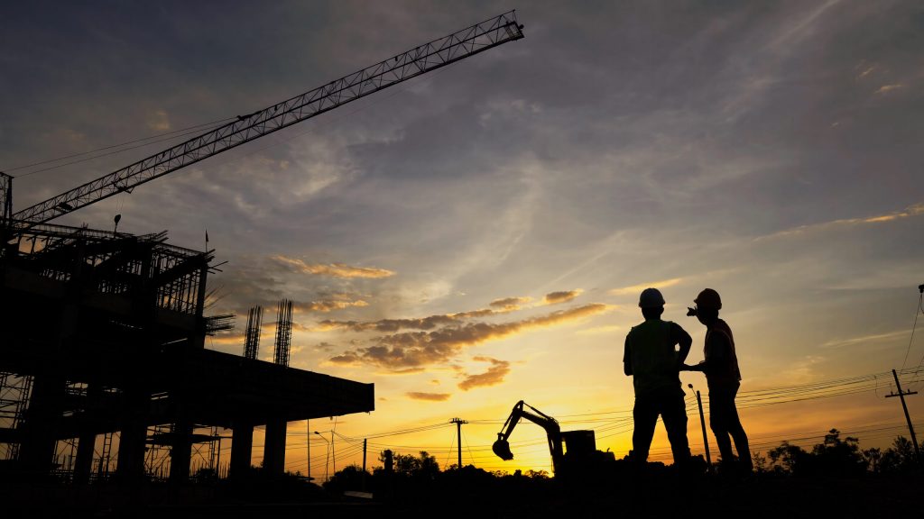 Entrée d’un site logistique au lever du soleil avec quelques silhouettes de travailleurs arrivant tôt