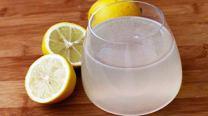 Verre d’eau légèrement trouble avec du jus de citron posé sur une table en bois, accompagné de citrons coupés et entiers, lumière naturelle douce, ambiance matinale calme, illustrant une boisson naturelle consommée au réveil