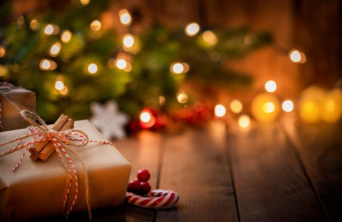 Paquet cadeau posé sur une table en bois devant un sapin décoré avec des lumières floues en arrière-plan.