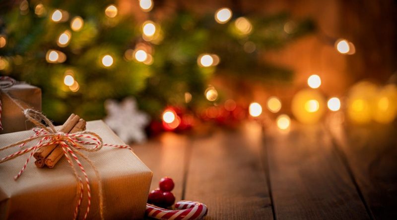 Paquet cadeau posé sur une table en bois devant un sapin décoré avec des lumières floues en arrière-plan.
