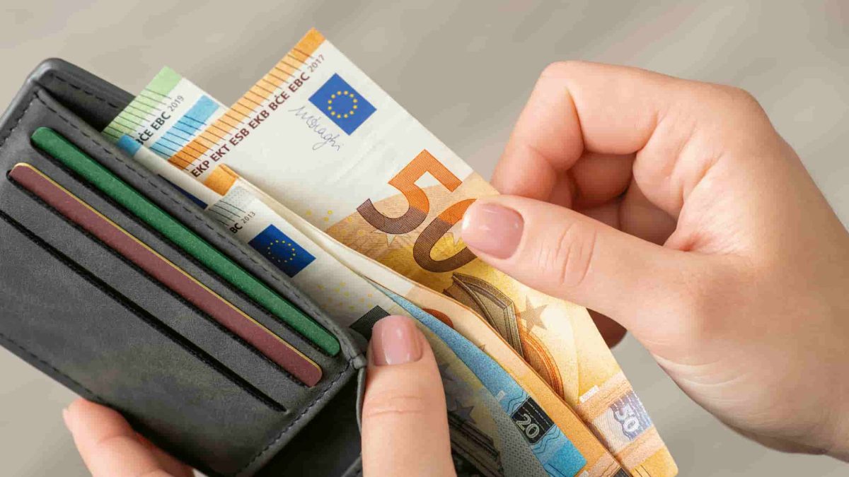 Main tenant un portefeuille ouvert avec plusieurs billets d’euros glissés à l’intérieur.