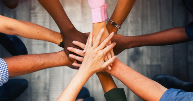 mains de personnes aux teintes de peau différentes posées les unes sur les autres, symbole d’égalité et de coopération