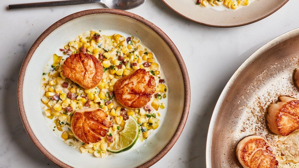 Assiette de noix dorées déposées sur un mélange crémeux de maïs, vue rapprochée dans une ambiance culinaire chaleureuse.