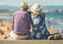 Couple de retraités assis face à la mer sur une promenade ensoleillée, profitant d’un cadre côtier paisible et d’un mode de vie détendu