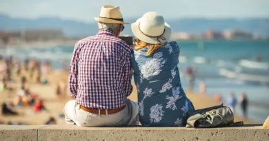Couple de retraités assis face à la mer sur une promenade ensoleillée, profitant d’un cadre côtier paisible et d’un mode de vie détendu