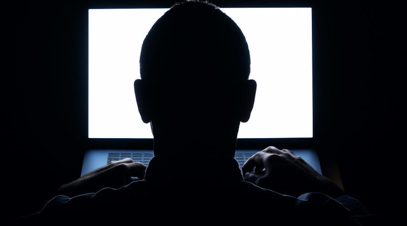 Silhouette d’une personne assise devant un écran d’ordinateur très lumineux dans une pièce sombre, symbolisant la recherche d’anonymat en ligne.