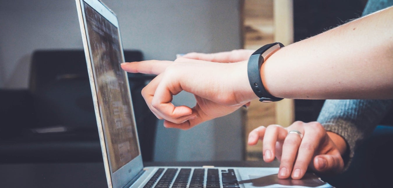 Mains pointant un écran d’ordinateur portable, illustrant une vérification en ligne ou une démarche administrative numérique.