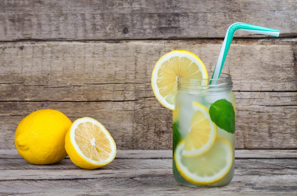 Verre d’eau fraîche avec des tranches de citron et quelques feuilles vertes, placé sur une table en bois.