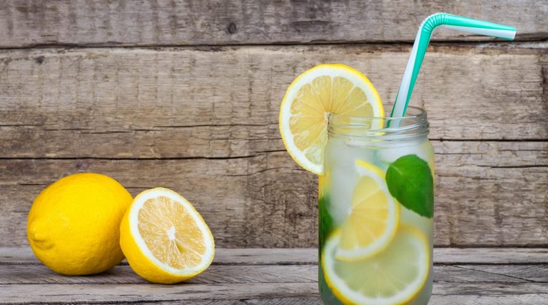Verre d’eau fraîche avec des tranches de citron et quelques feuilles vertes, placé sur une table en bois.