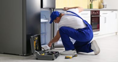 Technicien réparant un réfrigérateur en panne dans la cuisine d’un logement meublé, outil ouvert au sol