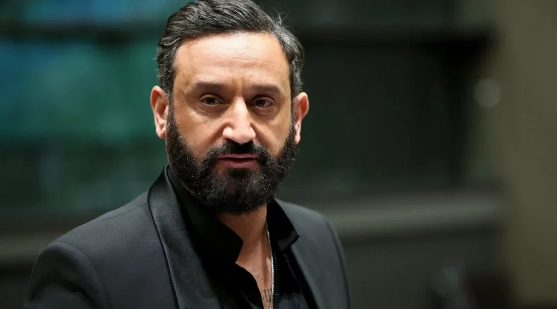 animateur de télévision barbu portant un costume sombre, regard sérieux, éclairage studio, ambiance de plateau télévisé en arrière-plan