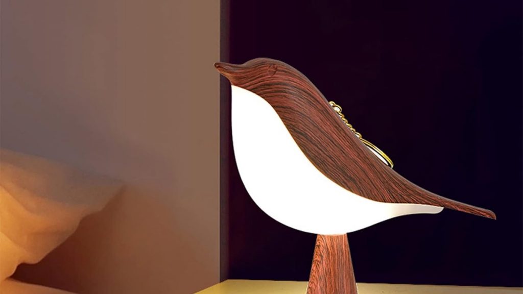 Lampe décorative en forme d’oiseau à l’aspect bois naturel, posée sur une table de chevet, révélant une structure lumineuse et électronique dissimulée derrière une apparence écologique.