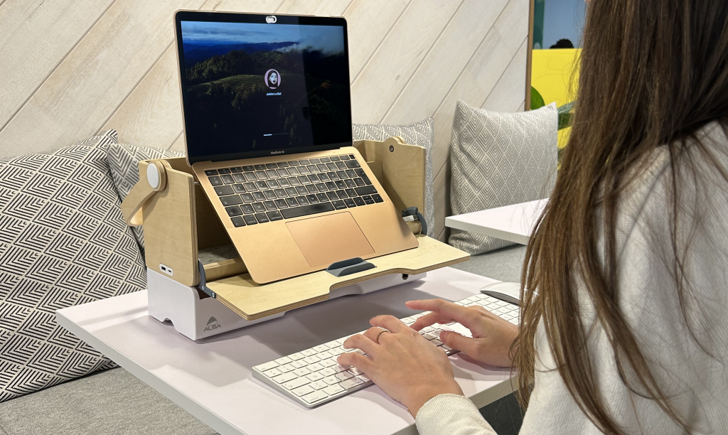 Personne travaillant sur un ordinateur portable posé sur un support en bois dans un espace de travail lumineux