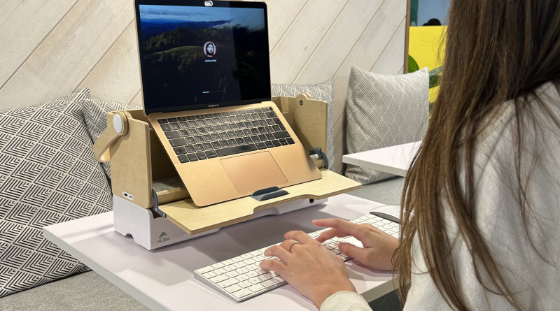 Personne travaillant sur un ordinateur portable posé sur un support en bois dans un espace de travail lumineux