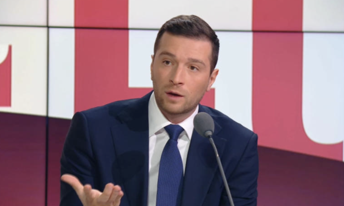 Homme politique en costume sombre s’exprimant sur un plateau de télévision lors d’un débat en direct, avec un geste de la main et une expression surprise