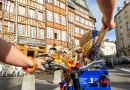 Personne circulant à vélo en libre-service dans une ville historique, guidon décoré de fleurs, scène de mobilité douce dans un centre urbain animé.