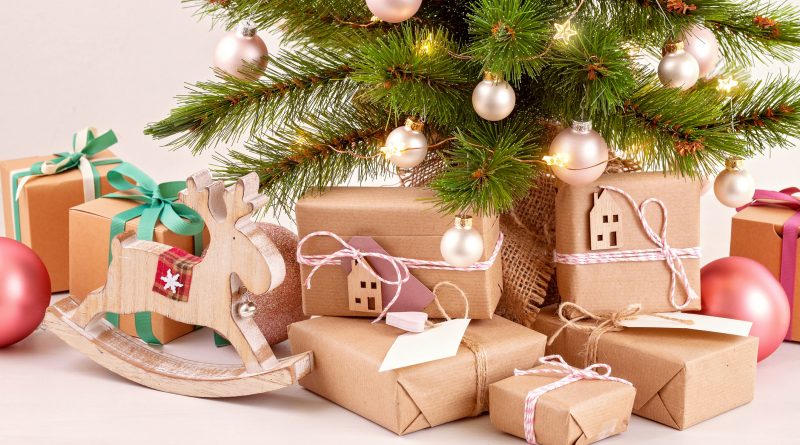 Pack de cadeaux emballés en papier kraft sous un sapin décoré de boules et lumières, avec une décoration en forme de renne en bois.