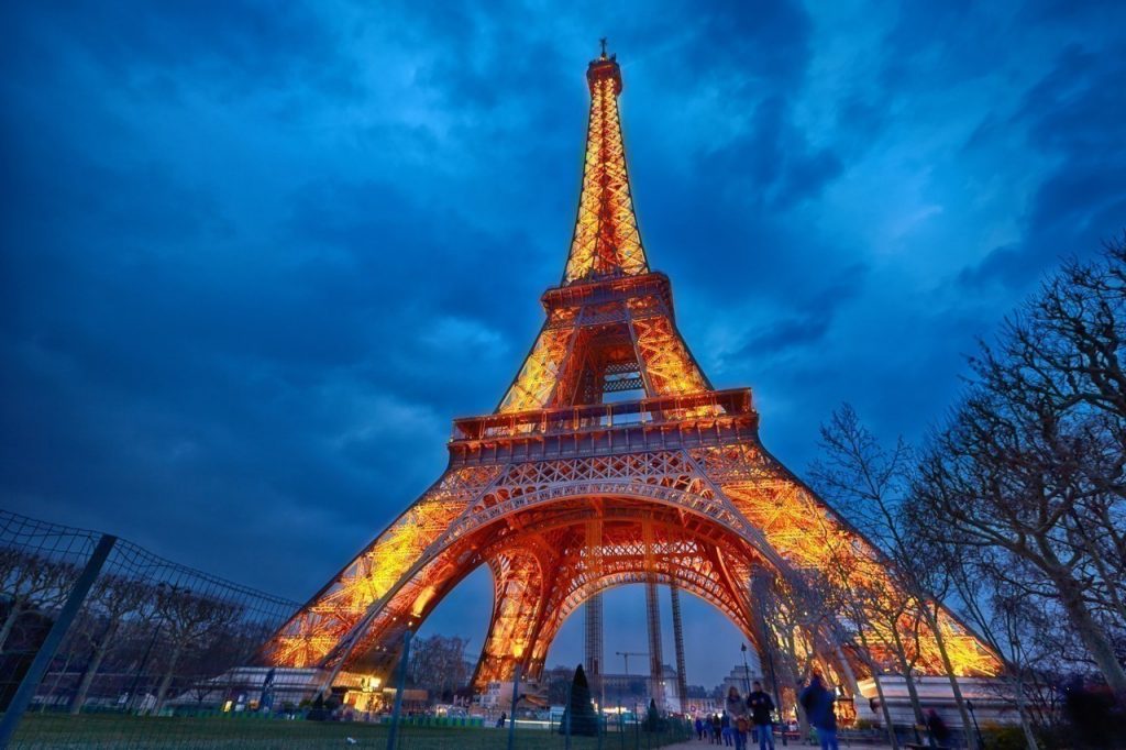 Monument illuminé de nuit avec une structure métallique dorée se détachant sur un ciel bleu profond.