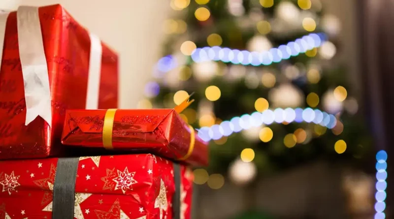 Cadeaux emballés en papier rouge posés au premier plan, avec un sapin illuminé en arrière-plan flou, évoquant les fêtes de fin d’année et les dépenses de Noël