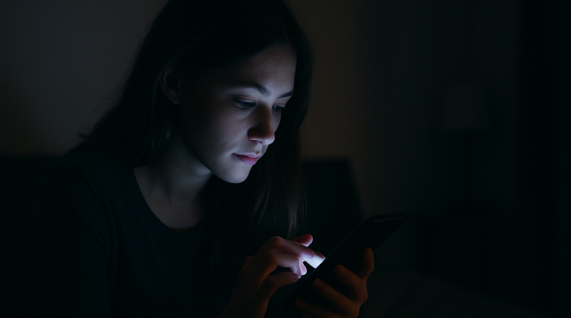 Personne seule utilisant un smartphone dans l’obscurité, visage éclairé par la lumière de l’écran dans une ambiance nocturne intime